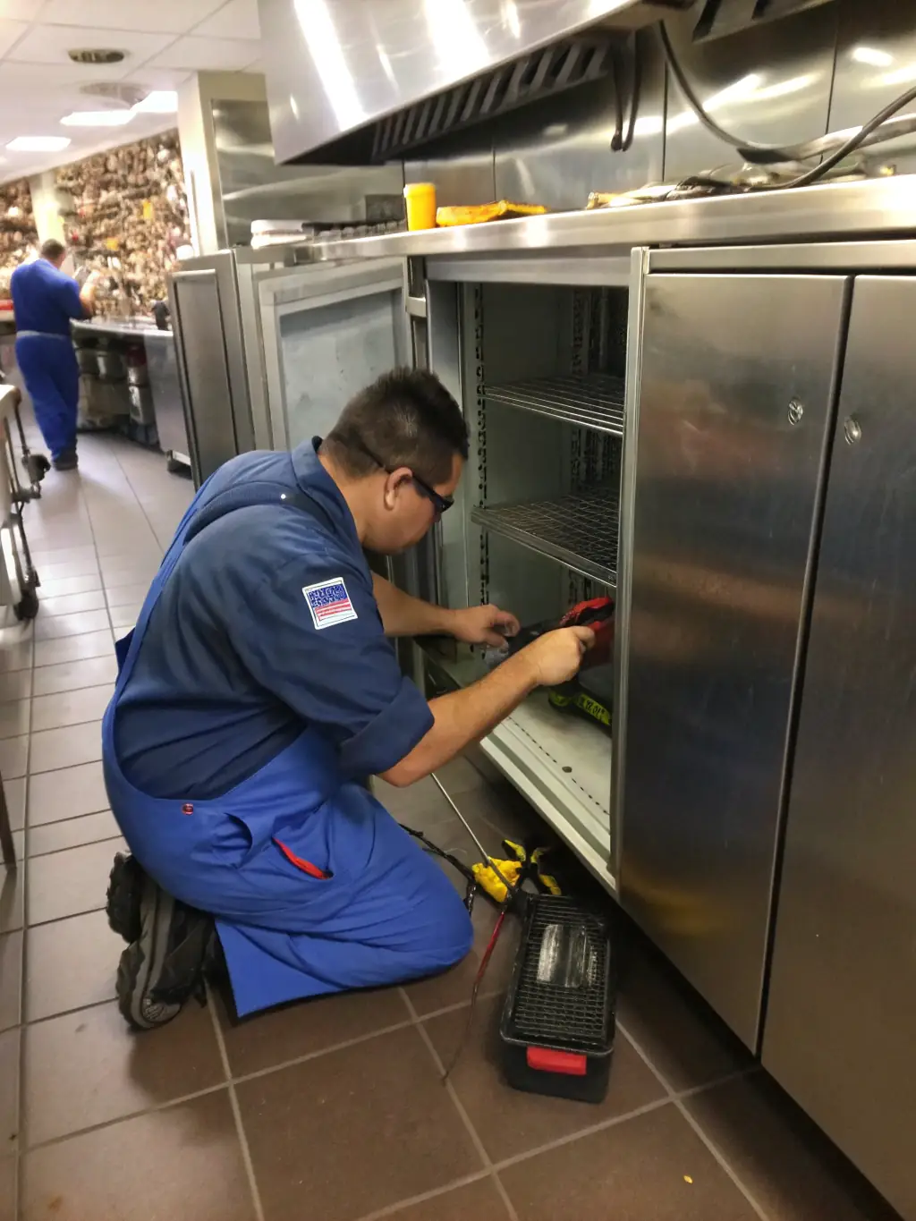 A close-up shot of a technician meticulously cleaning the coils of a commercial refrigeration unit in a restaurant kitchen, emphasizing the detail and care taken during maintenance.